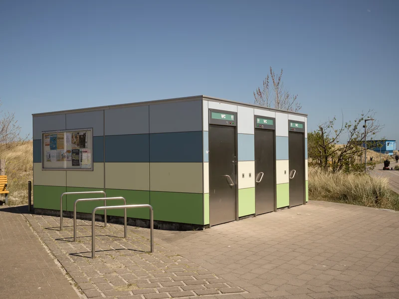Colorful public restroom building with a bicycle rack and yellow bench in a park setting.