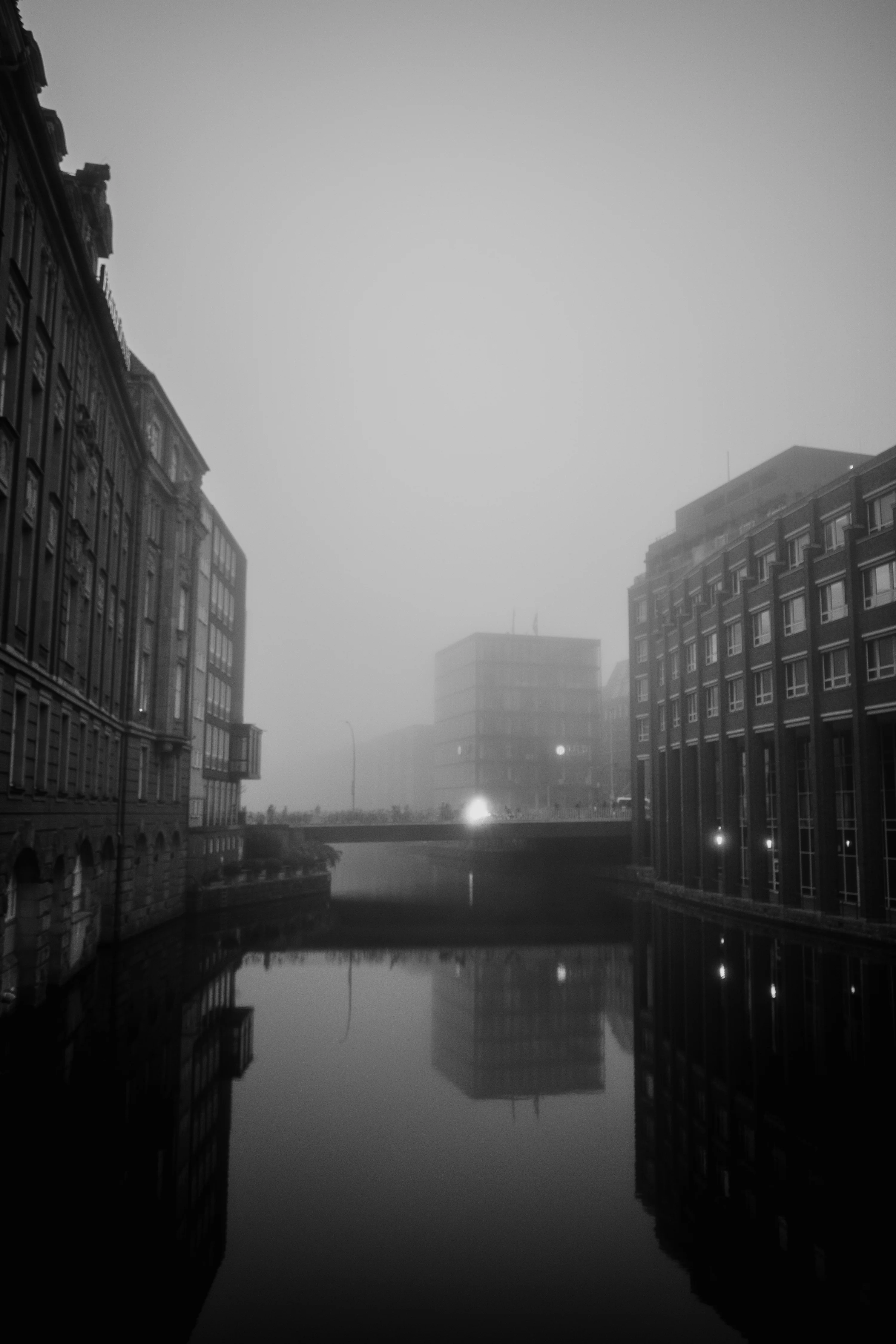 Foggy cityscape with buildings and their reflections in a canal.