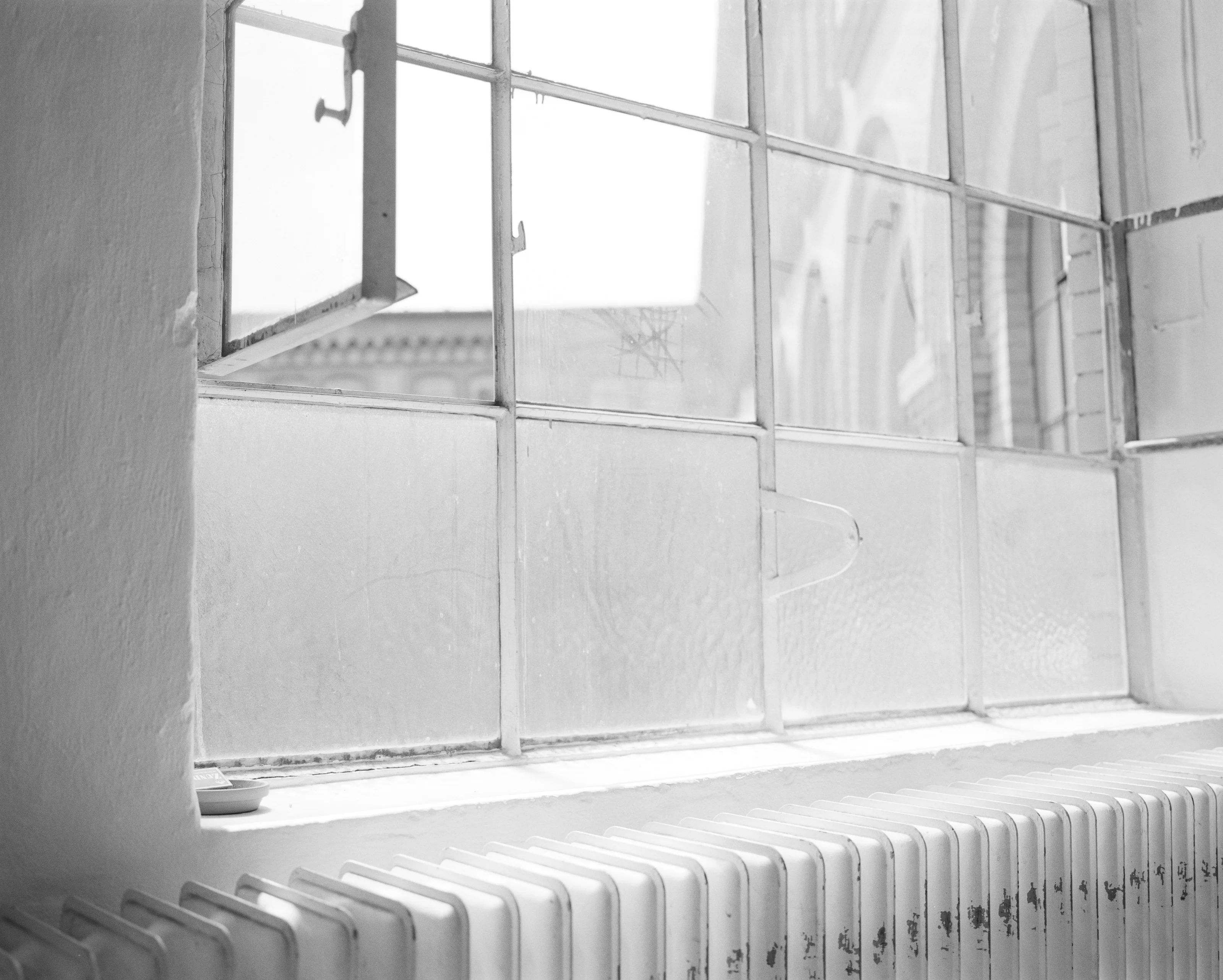 A black and white photo of a radiator beneath a large, multi-paned window with an open section.