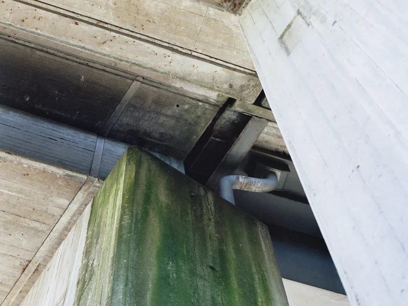 Concrete architecture with a green-stained pillar and overhead beams.