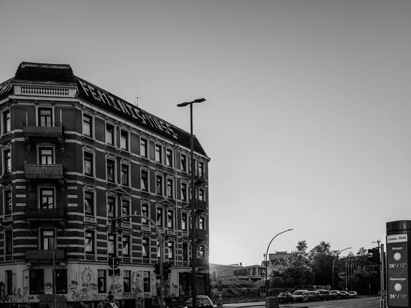 A multi-story building with graffiti at its base and a nearly empty street beside it under a clear sky.