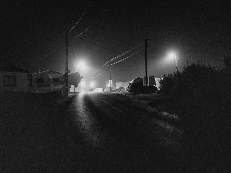 A nighttime street scene with streetlights illuminating a quiet road and silhouetted buildings.