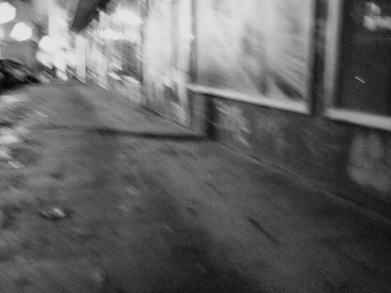Blurred black and white image of an urban street at night.