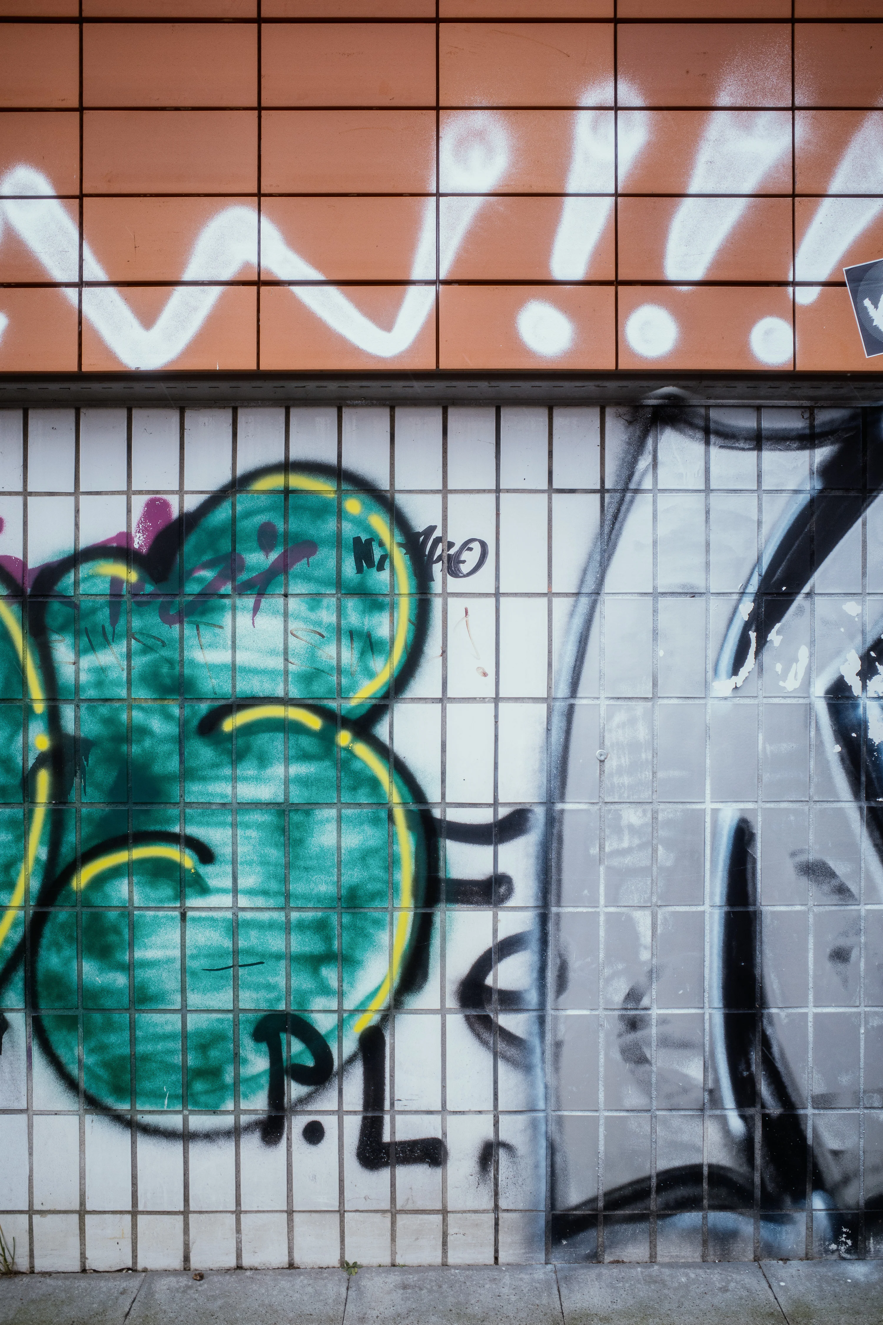 Graffiti on tiled wall with large green and gray shapes and orange background.
