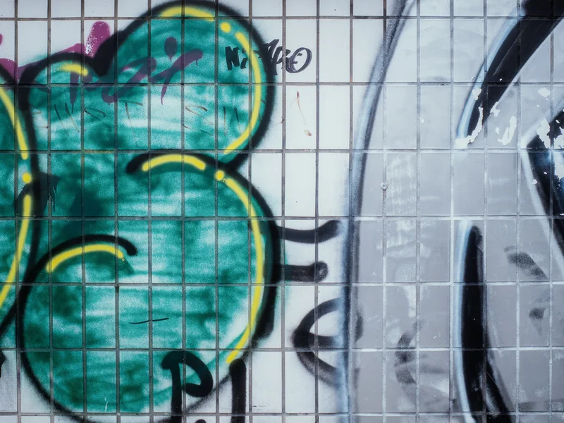 Graffiti on tiled wall with large green and gray shapes and orange background.