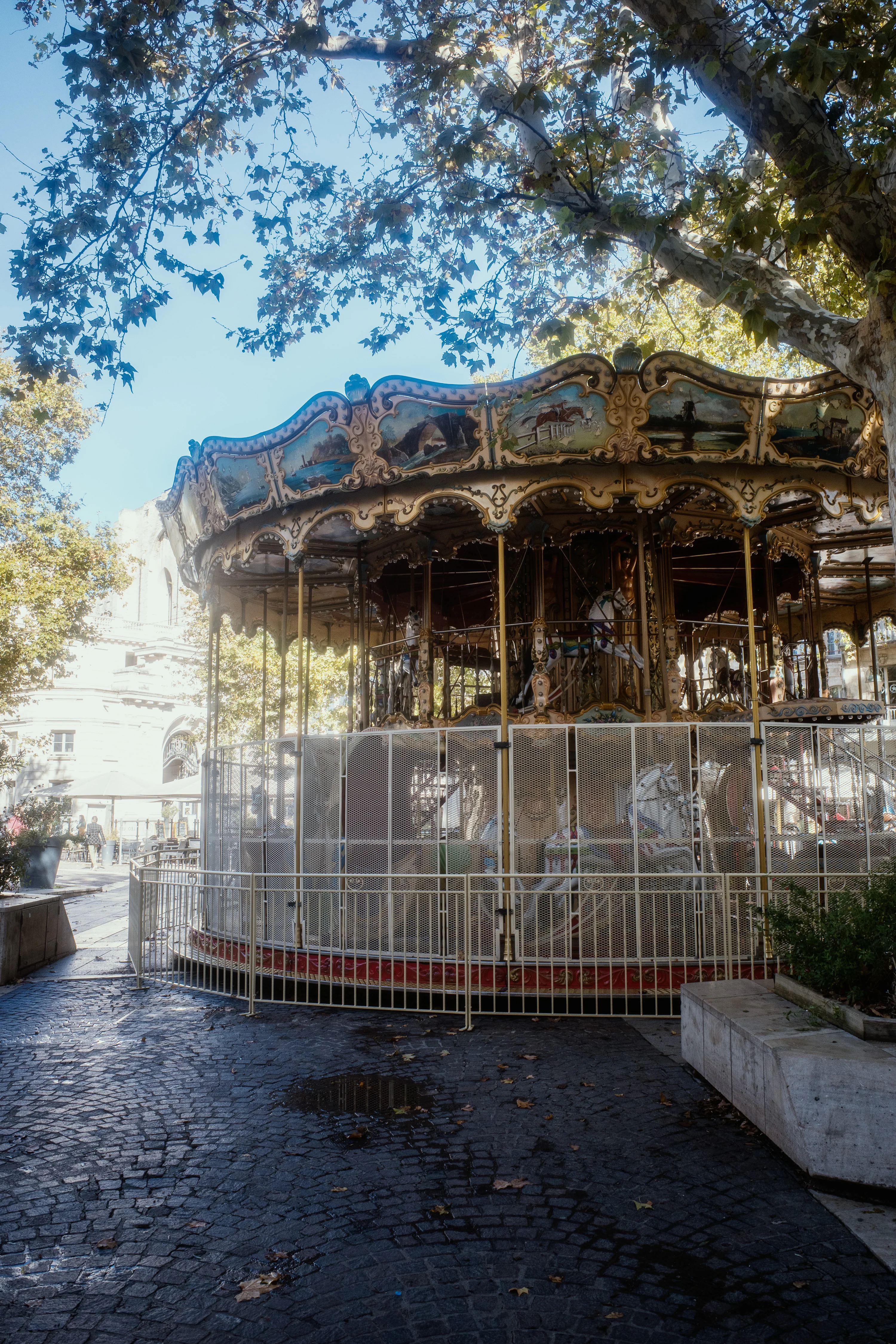 A vintage carousel under the shade of trees in an outdoor setting.