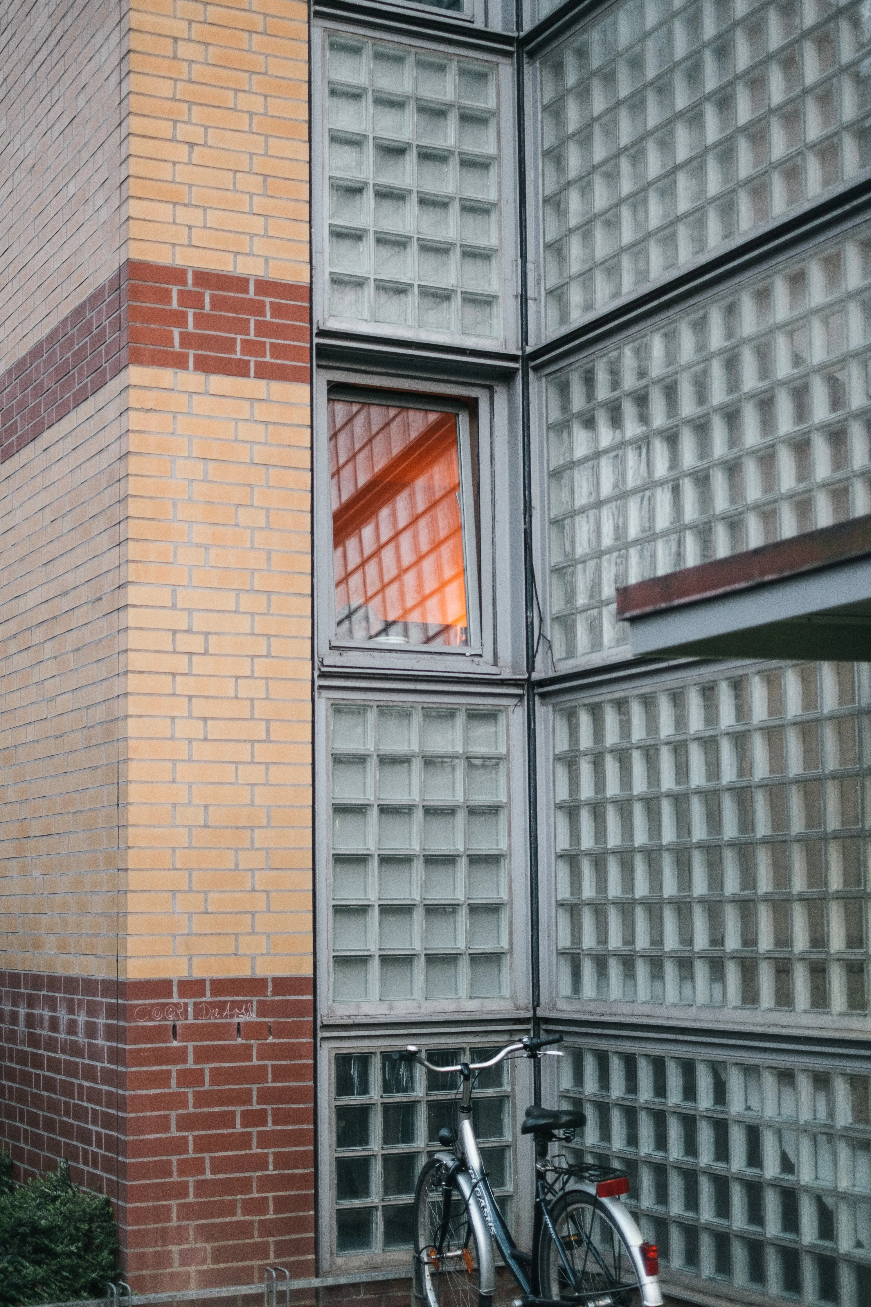 Bicycle parked against a building with a brick design and glass block windows reflecting orange light.