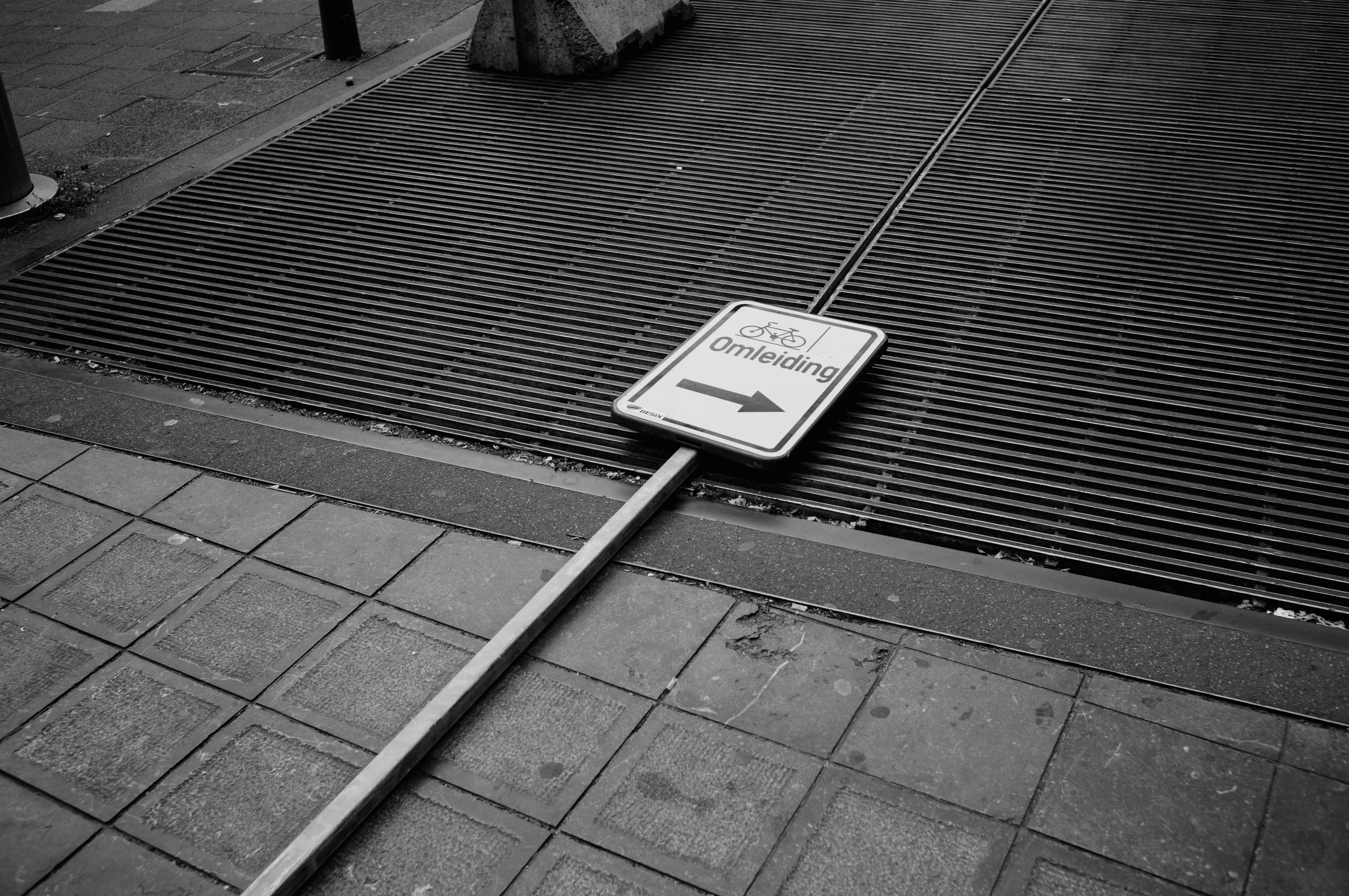 A fallen road sign with the word 'Omleiding' on a metal grate.