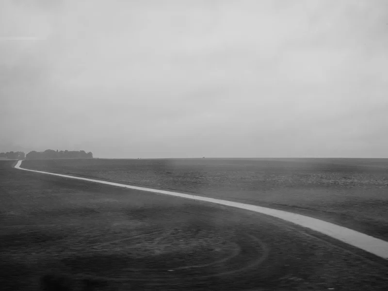 A winding path cuts through a vast, empty landscape under a cloudy sky.