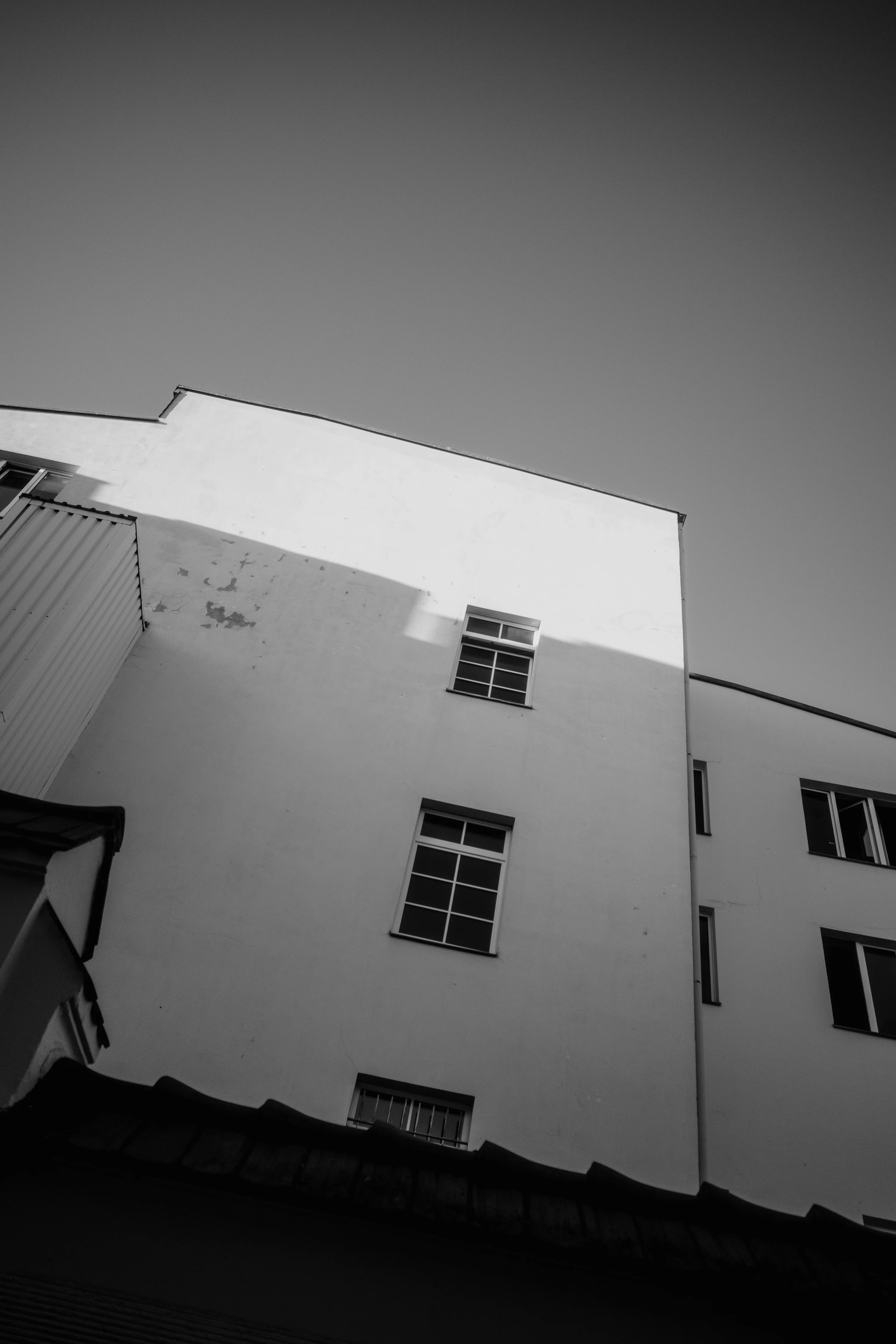 Black and white photo of a building facade with windows and shadows under a clear sky.