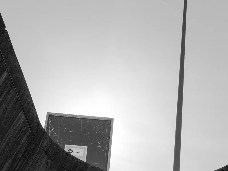 A street light and a billboard partially obscured by a curved concrete wall under a clear sky.