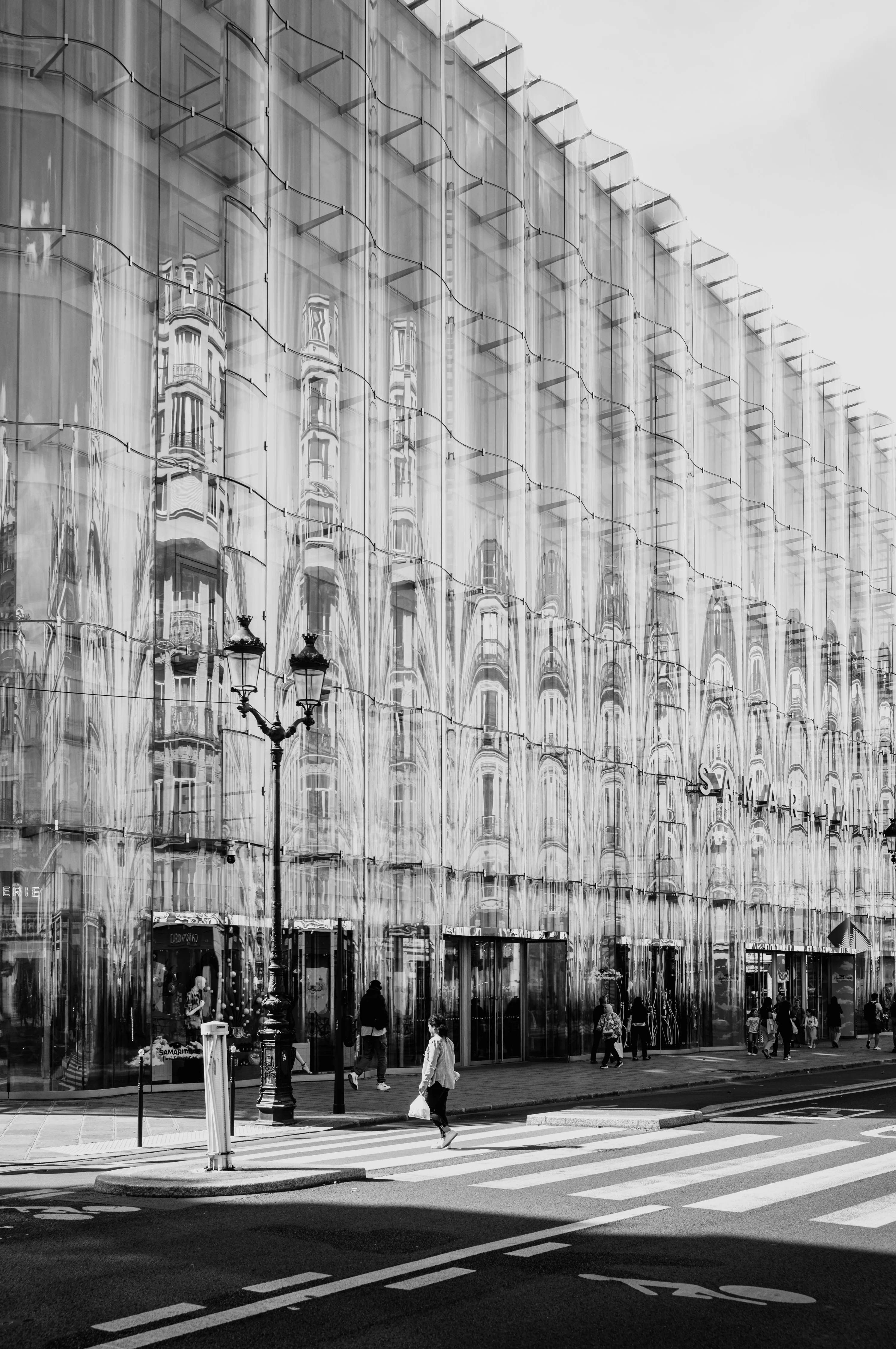 Black and white photo of a street scene with a modern glass building reflecting older architecture.