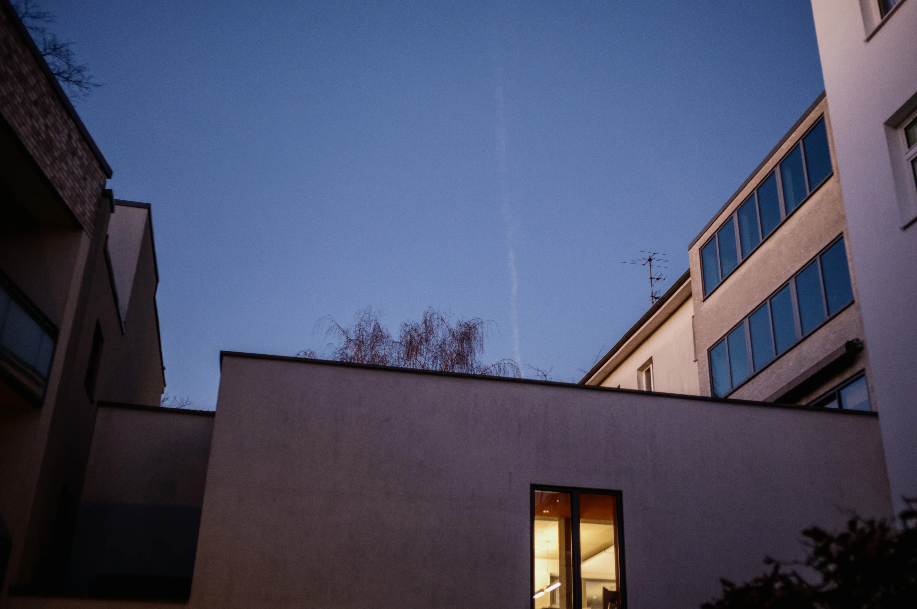 Evening view of a building courtyard with a lit window against a clear sky.