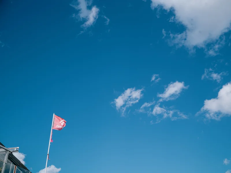 A red flag flying against a clear blue sky with scattered clouds.