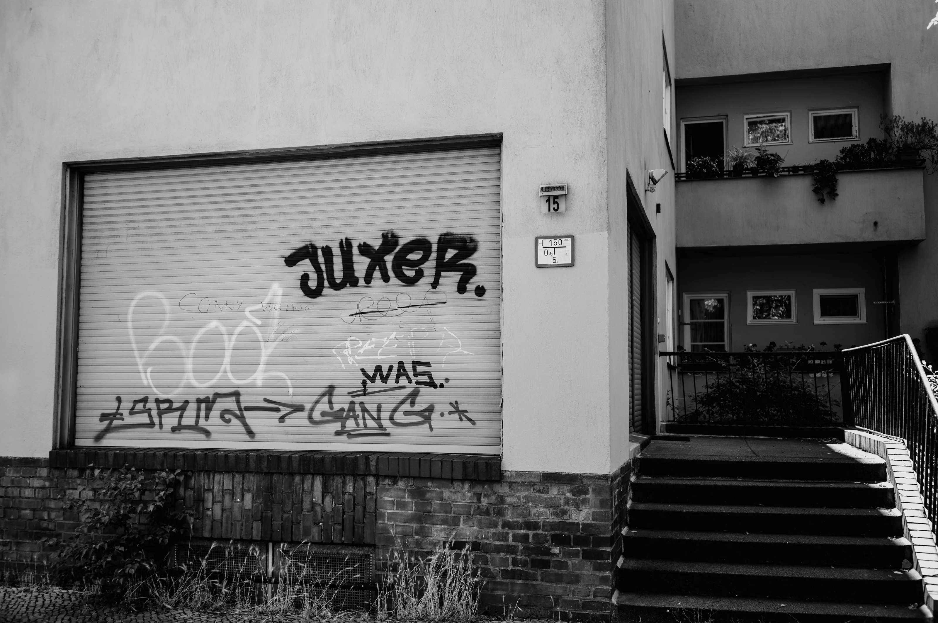 A building facade with graffiti on a roller shutter and adjacent staircase.