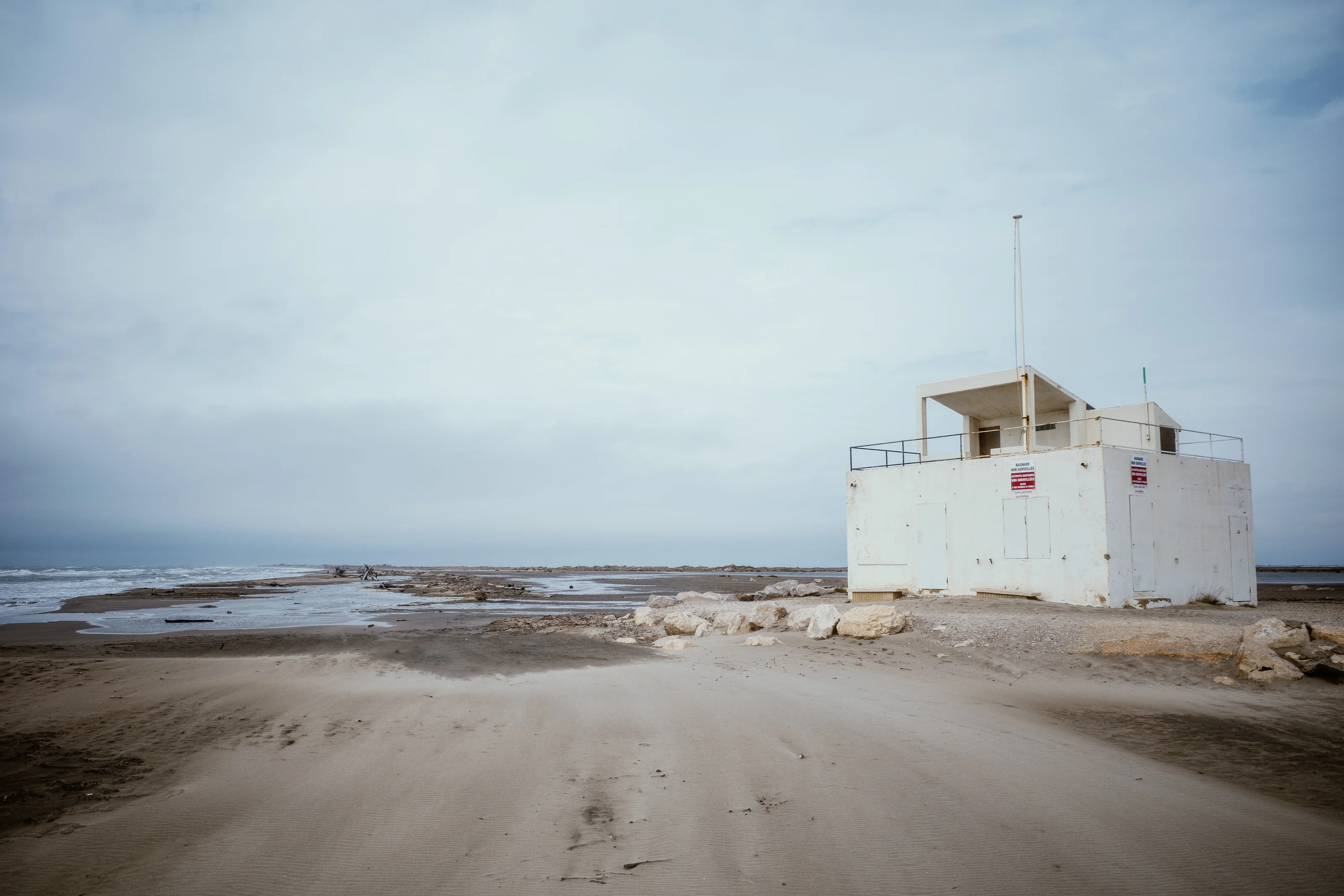 A white lifeguard tower stands on a deserted beach with overcast skies.