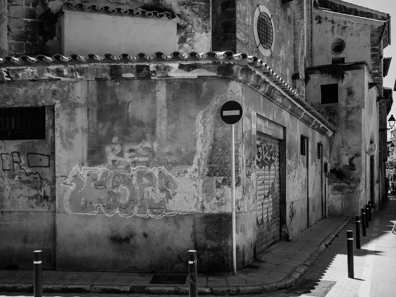 A weathered building with graffiti and a no-entry sign on a narrow street.
