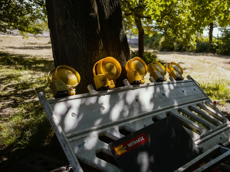 A row of yellow construction lights resting on a metal barricade under a tree.