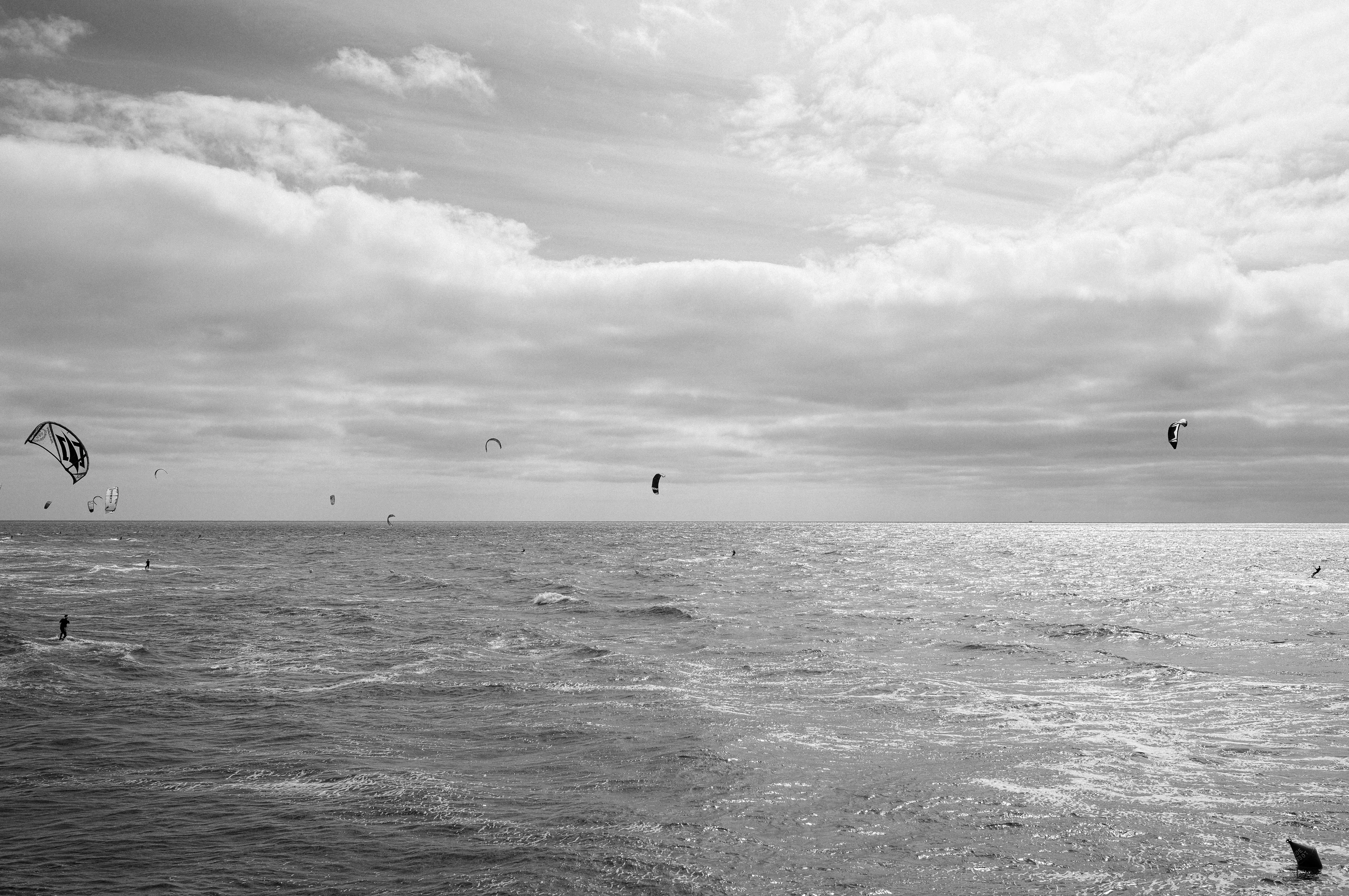 Several kitesurfers on a vast ocean under a cloudy sky.