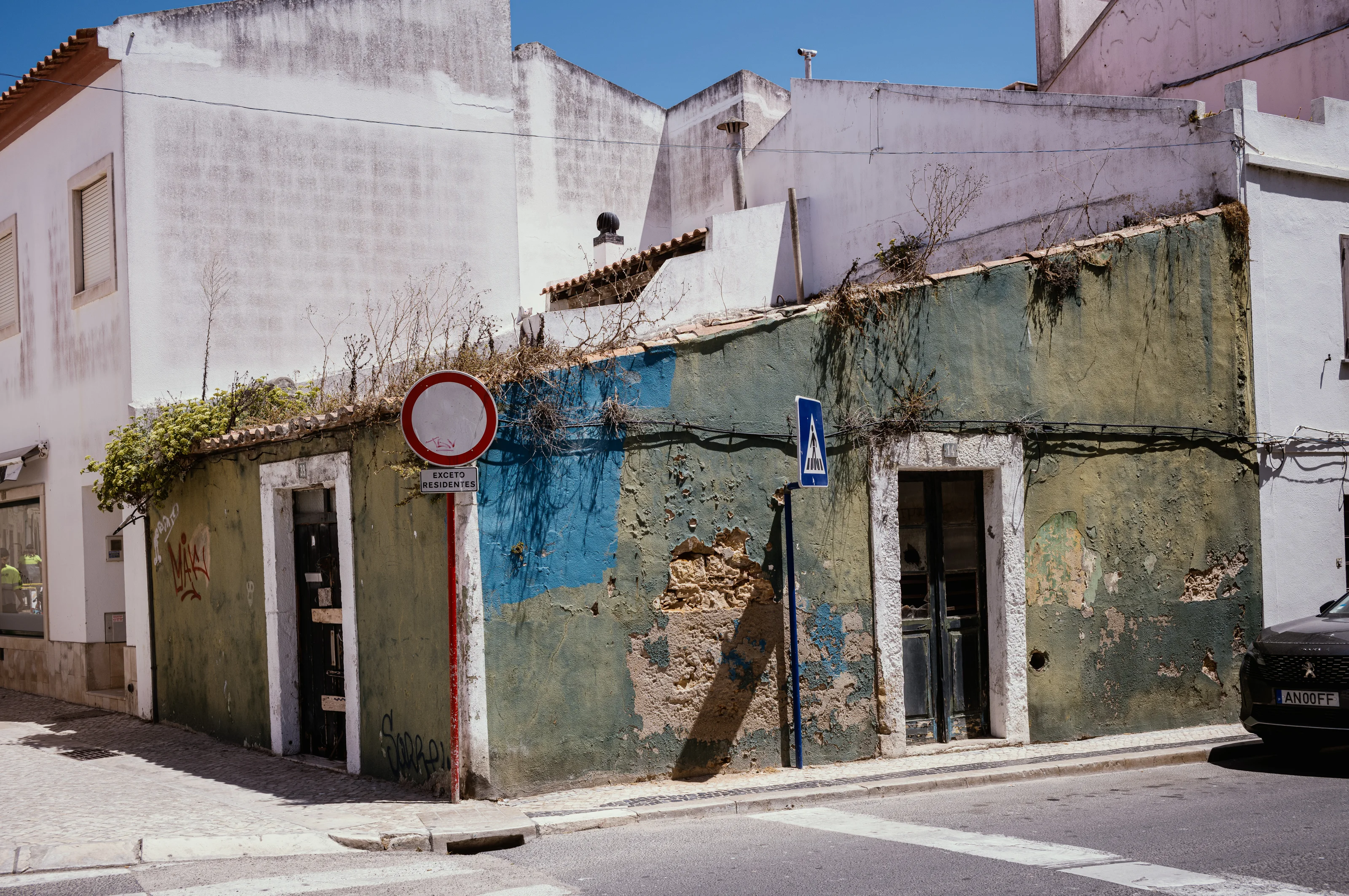 A worn, colorful wall of a building with a round traffic sign and a pedestrian crossing sign in an urban setting.