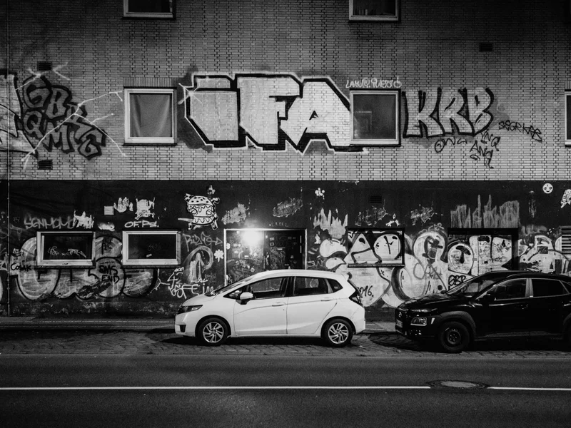 Two parked cars in front of a graffiti-covered building at night.