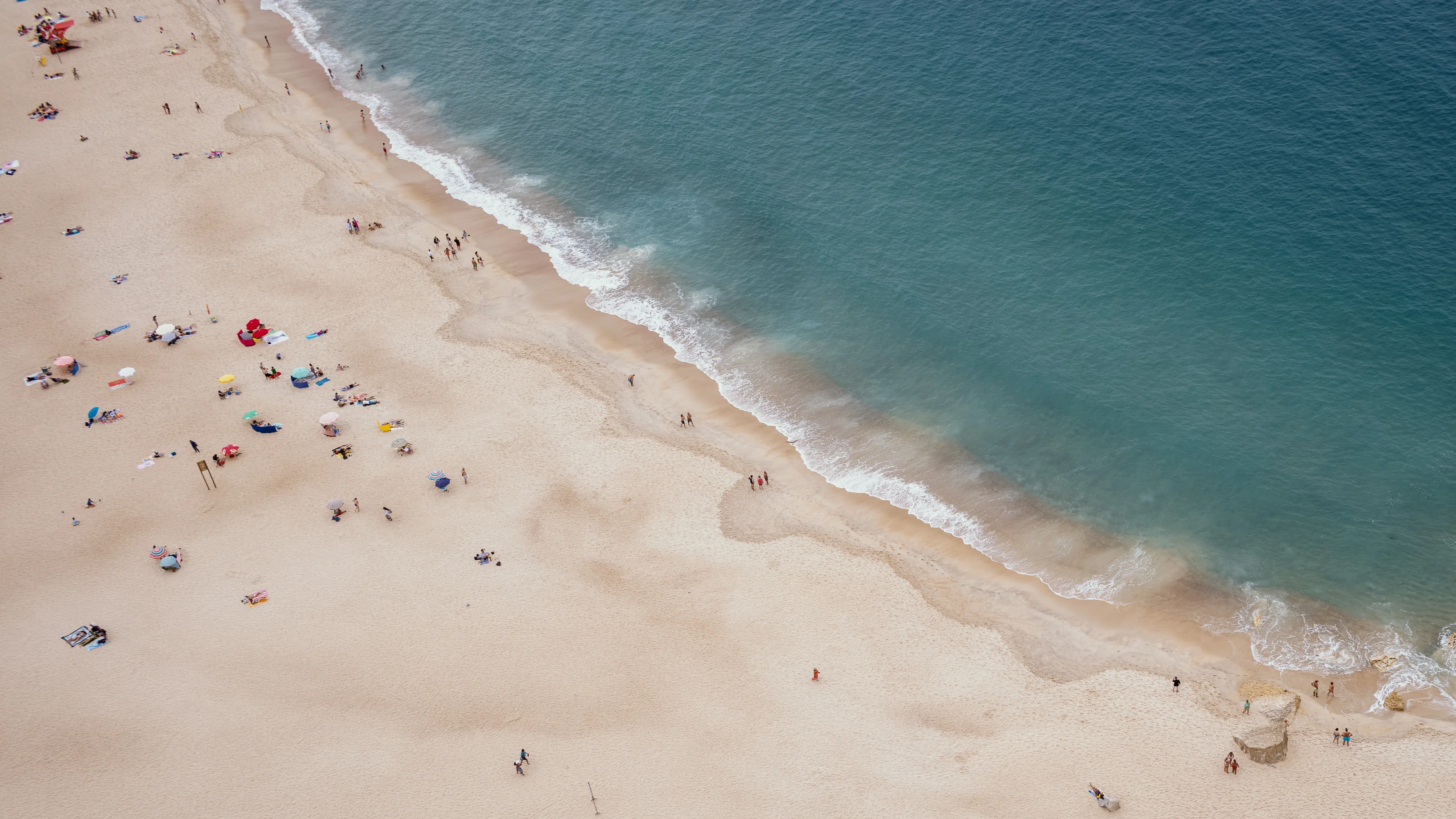 Aerial view of a busy beach with people, umbrellas, and waves meeting the shore.
