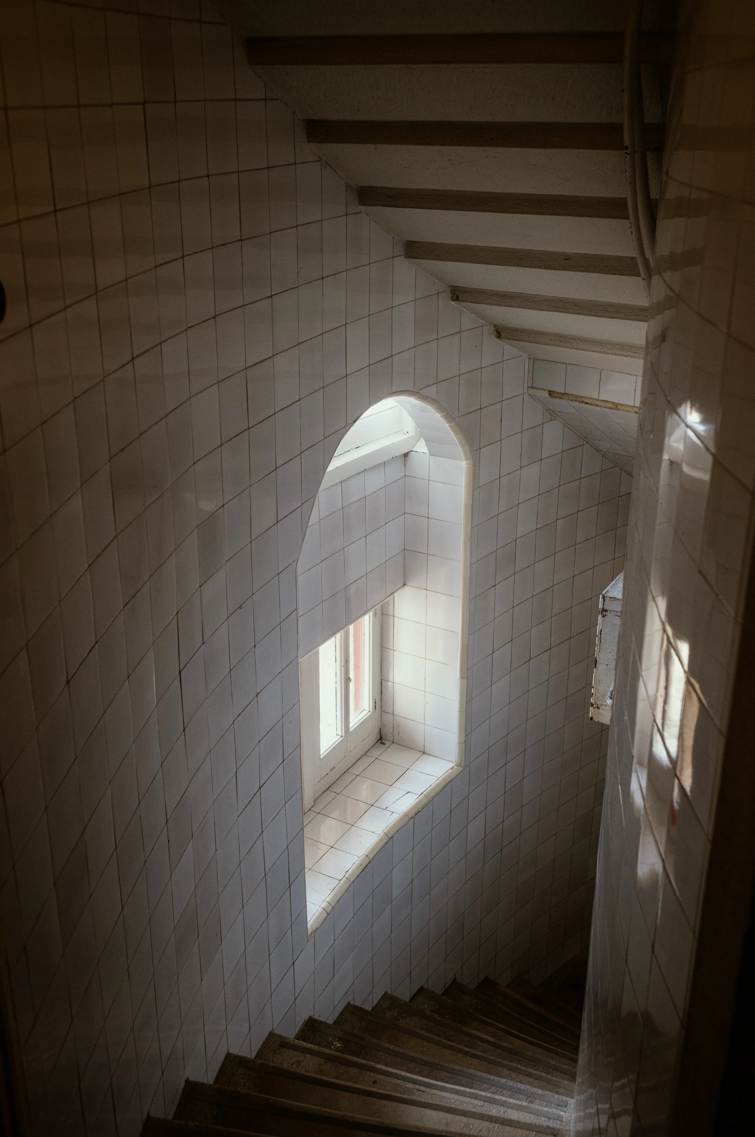 A spiral staircase with tiled walls and a window at the landing.
