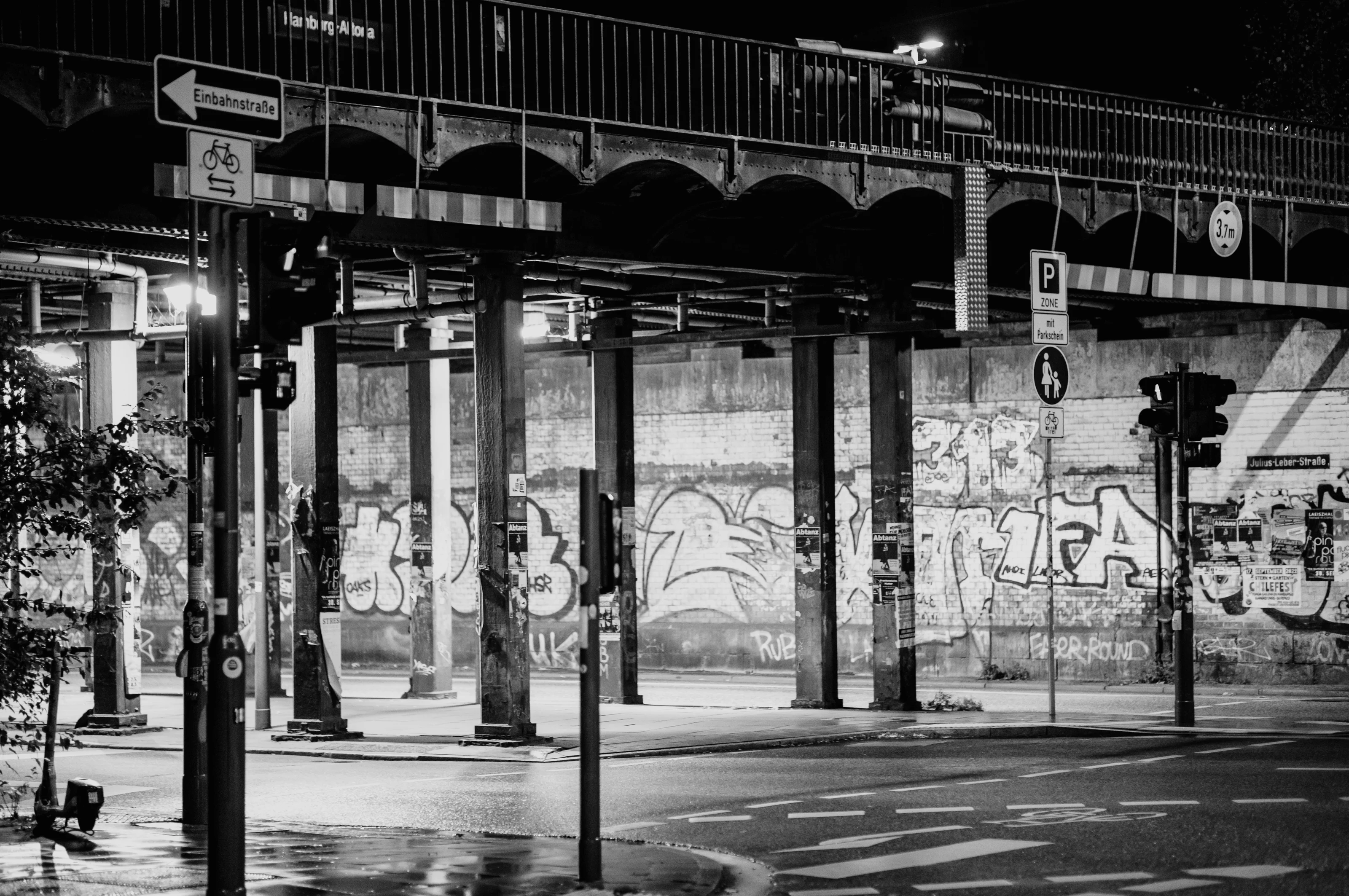 Black and white urban scene with graffiti-covered walls under an overpass at night.