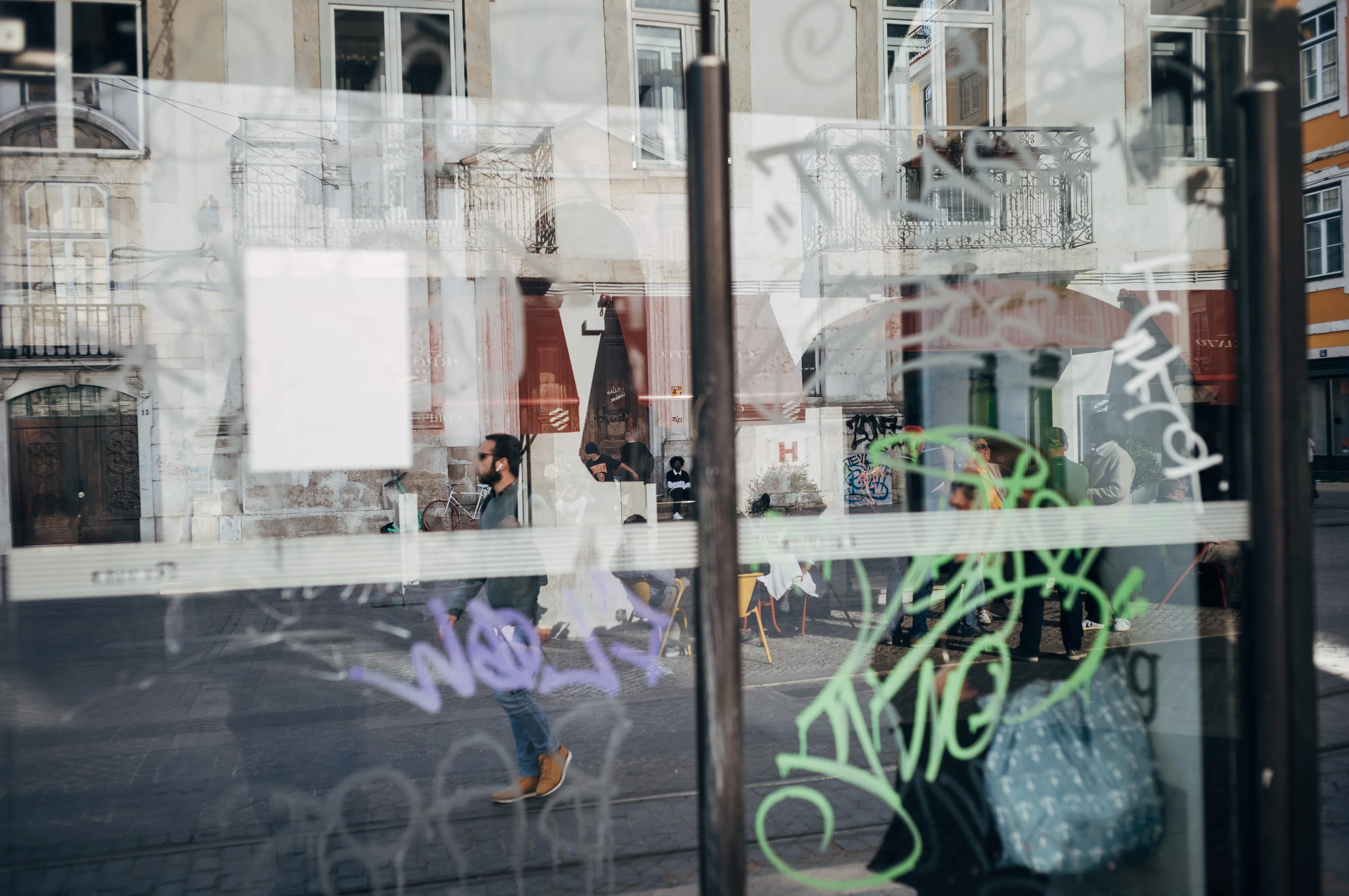 Reflection of urban street scene with graffiti on glass and people walking.