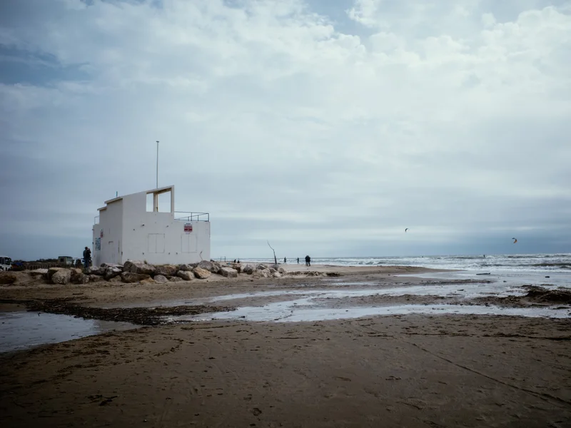 A white building on a rocky beach under a cloudy sky.