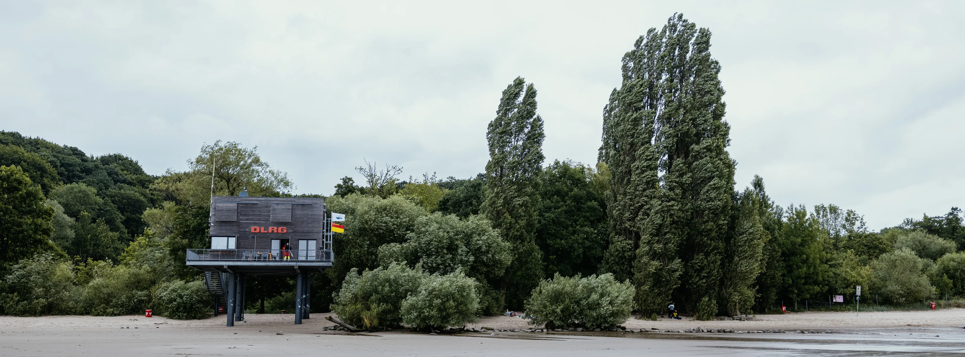 A lifeguard station on stilts near a beach, surrounded by trees.