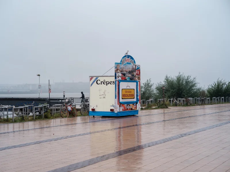 A closed crepe stall on a rainy boardwalk with bicycles nearby.