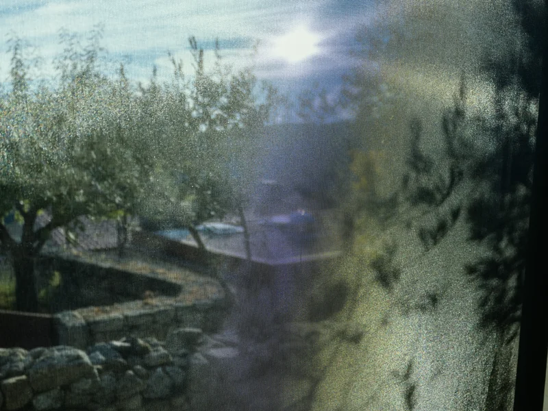 Sunlight filtering through a mesh curtain with trees and a stone wall outside.