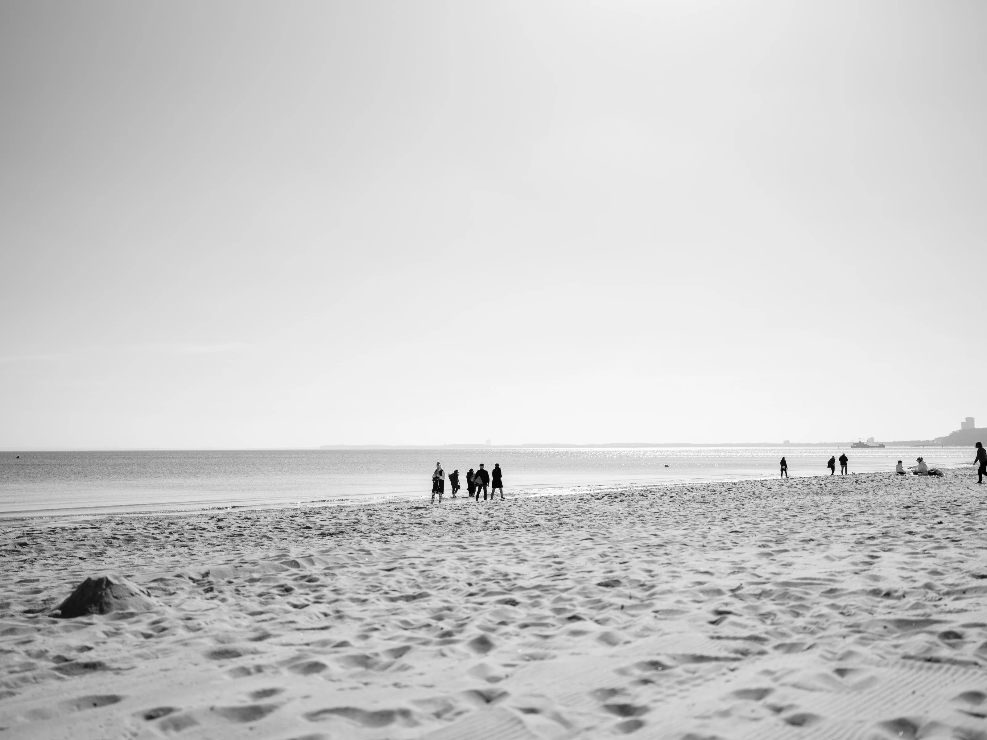 People walking along a sandy beach with calm sea and distant horizon.