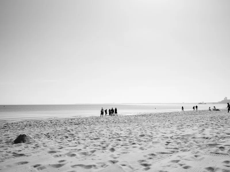 People walking along a sandy beach with calm sea and distant horizon.