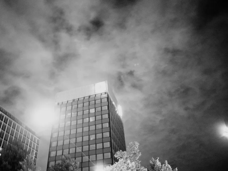 Black and white photo of tall, modern buildings with cloudy sky overhead.